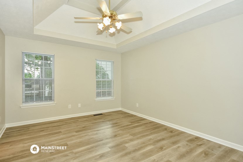 the spacious living room with hardwood flooring and a ceiling fan