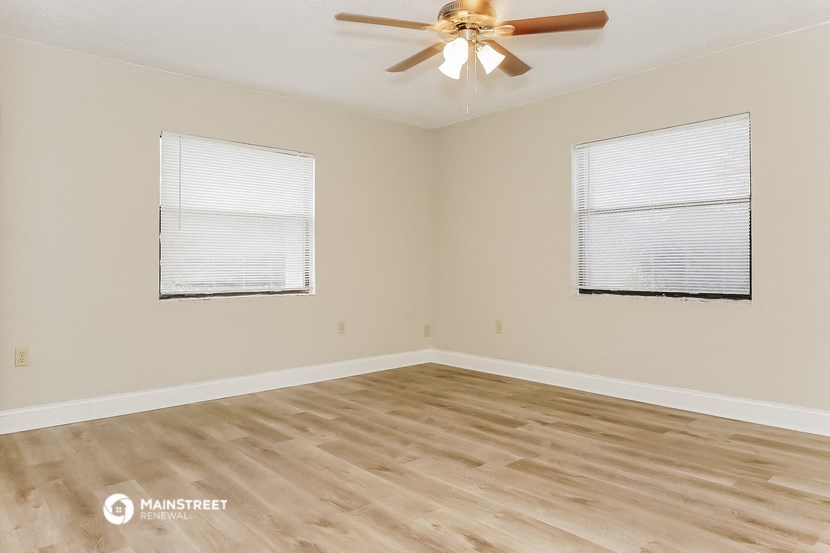 the spacious living room with two windows and a ceiling fan
