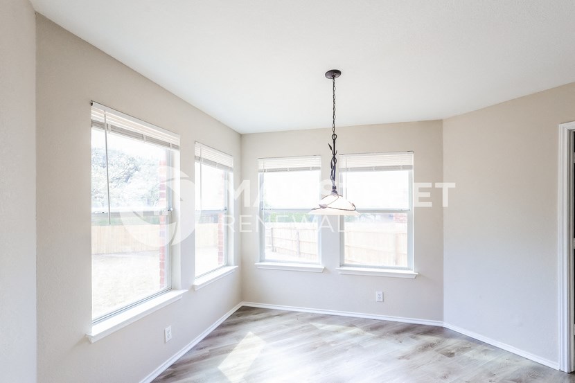 an empty living room with three windows and a chandelier