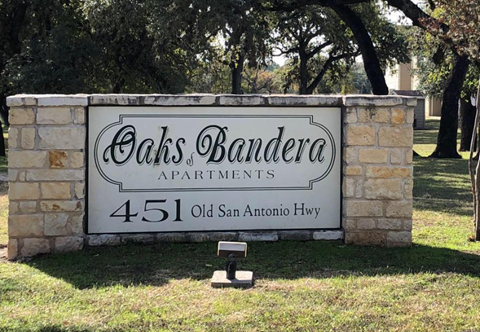 a sign for oaks bandeau apartments in front of trees