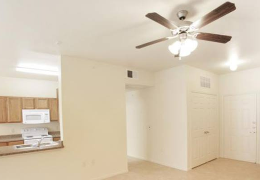an empty living room with a ceiling fan and a kitchen