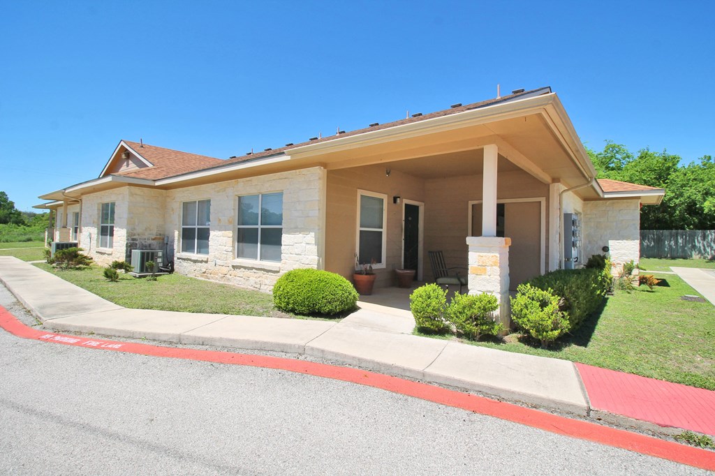 a tan house with a porch and a sidewalk in front of it