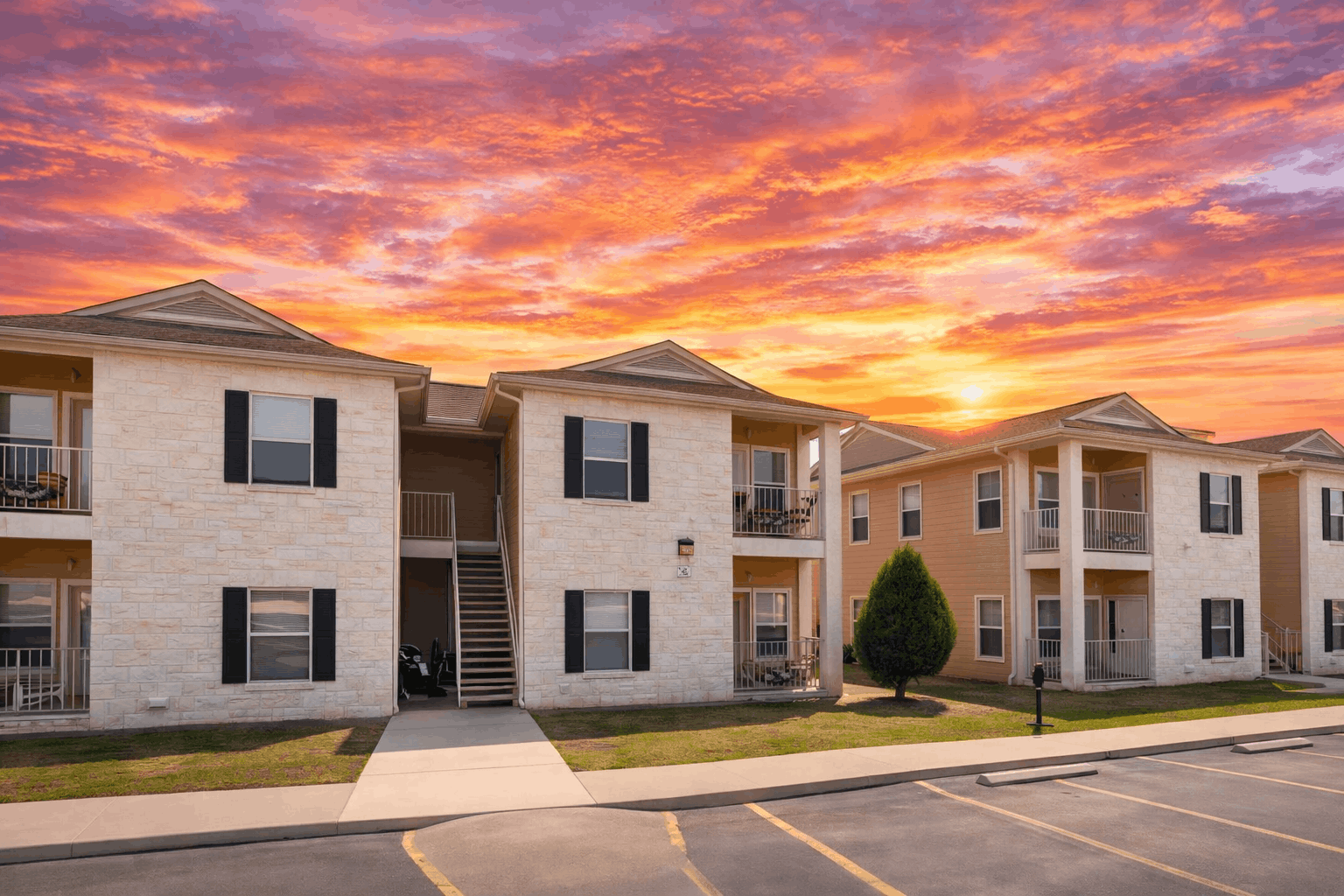 A sunset view of apartment buildings with a parking lot in the foreground.