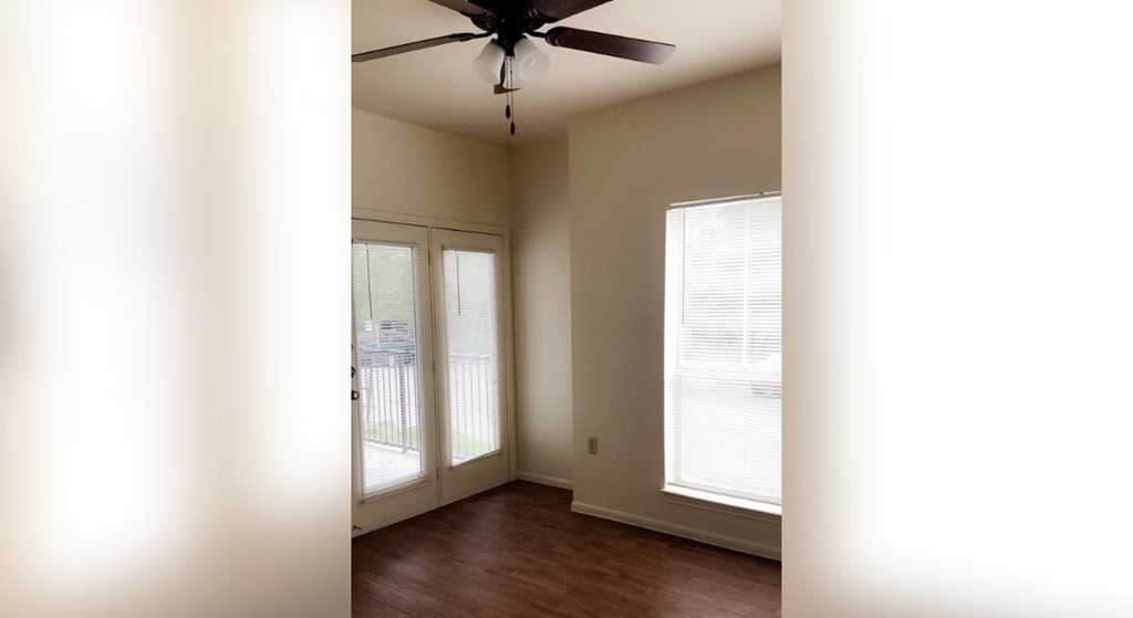 an empty living room with a ceiling fan and windows
