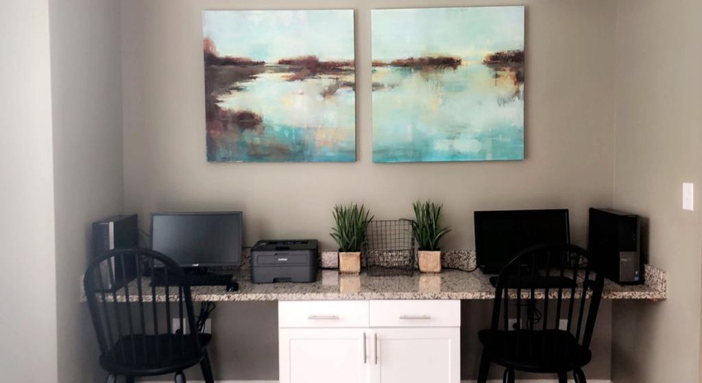 two paintings on the wall above an office desk with chairs