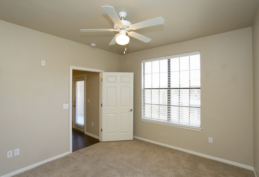 an empty living room with a ceiling fan and a window