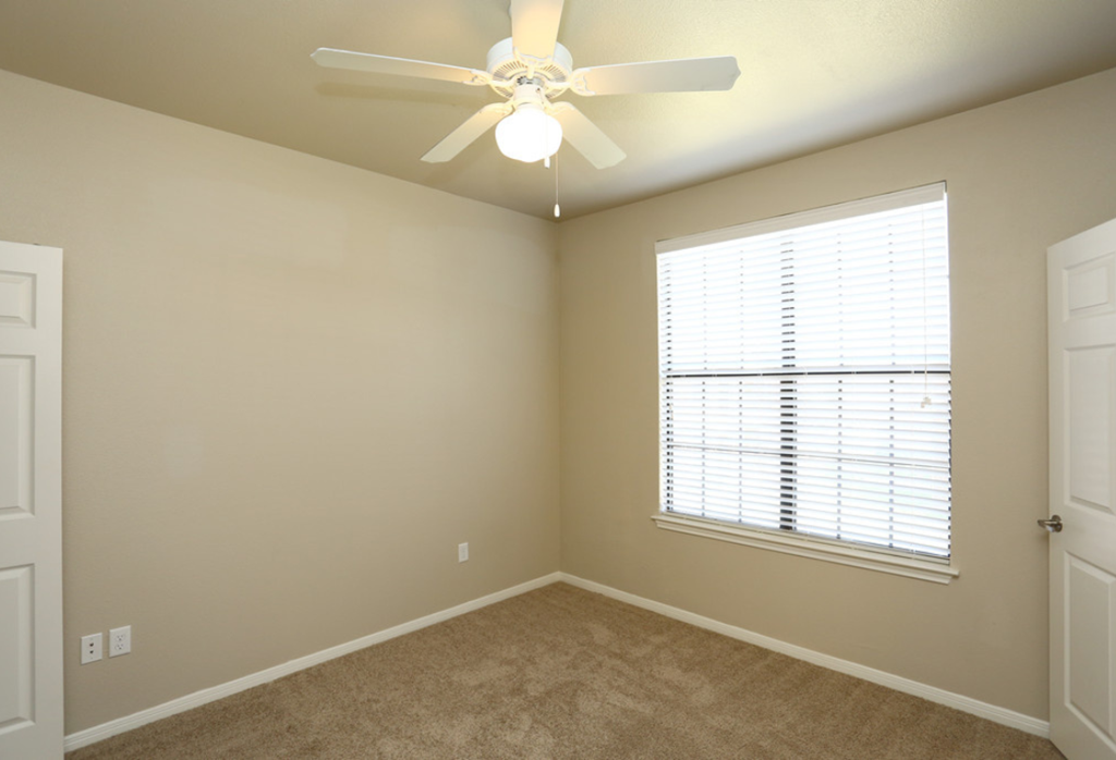an empty bedroom with a ceiling fan and a window