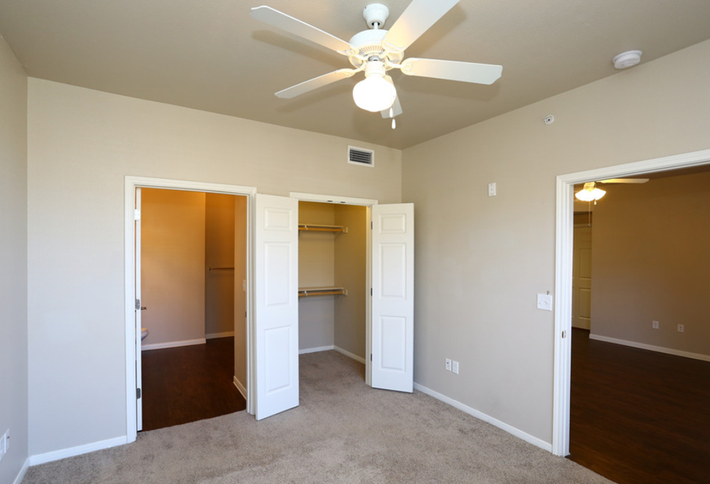an empty living room with a ceiling fan and a closet