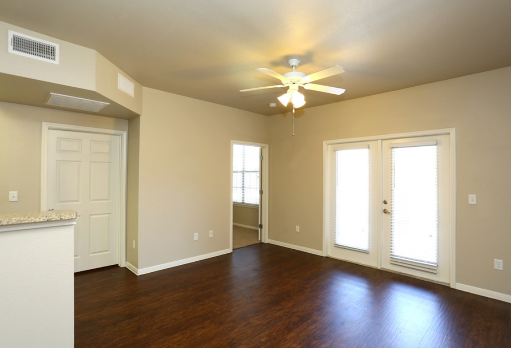 an empty living room with wood floors and a ceiling fan