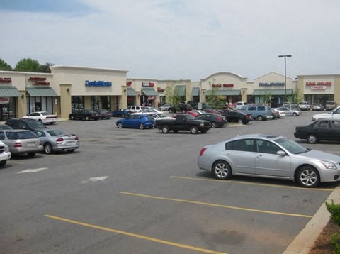 A parking lot with cars and storefronts in the background.