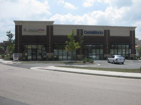 A white car is parked in front of a dental office.