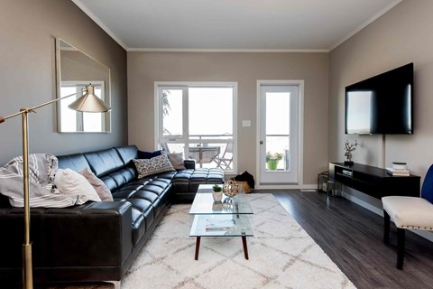 A living room with a black leather couch, a glass coffee table, and a flat-screen TV mounted on the wall.