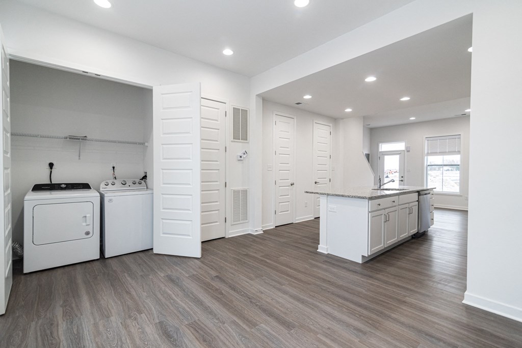 an open kitchen and laundry room with white appliances and wooden floors