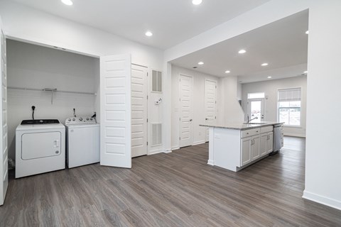 an open kitchen and laundry room with white appliances and wooden floors