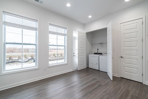 an empty living room with white walls and wood floors and a laundry room with windows