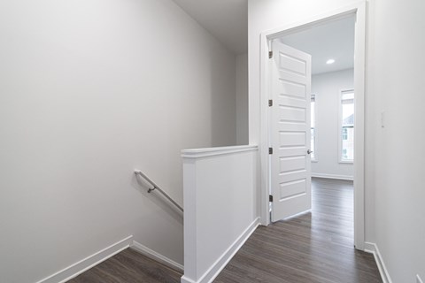 a corridor in a home with a white door and a staircase