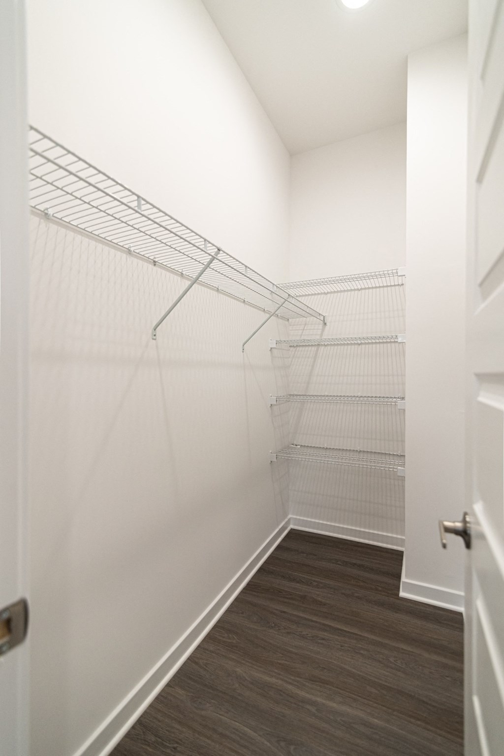 a walk in closet in a bedroom with white walls and a wood floor