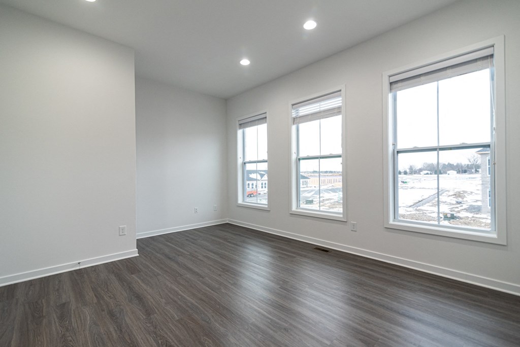 an empty living room with wood floors and three windows