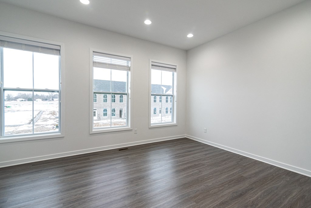 an empty living room with wood flooring and three windows