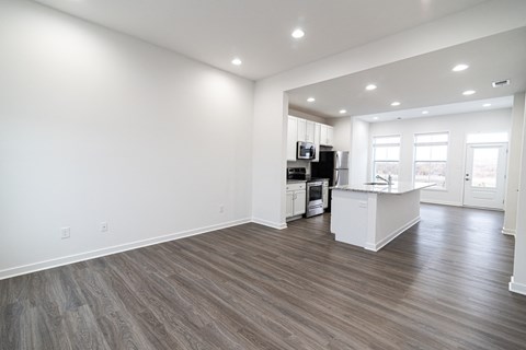 an empty living room and kitchen with white walls and wood flooring