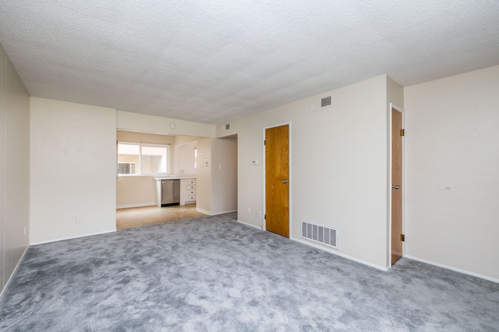 an empty living room with a door to a kitchen