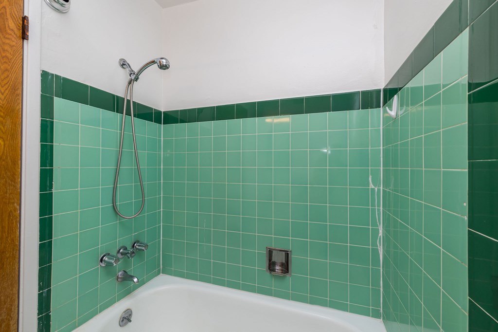 a green tiled bathroom with a tub and a shower