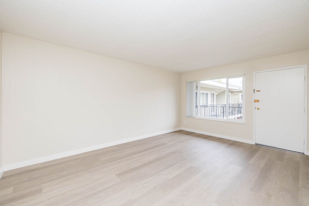 A room with a white door and a window with a view of a balcony.