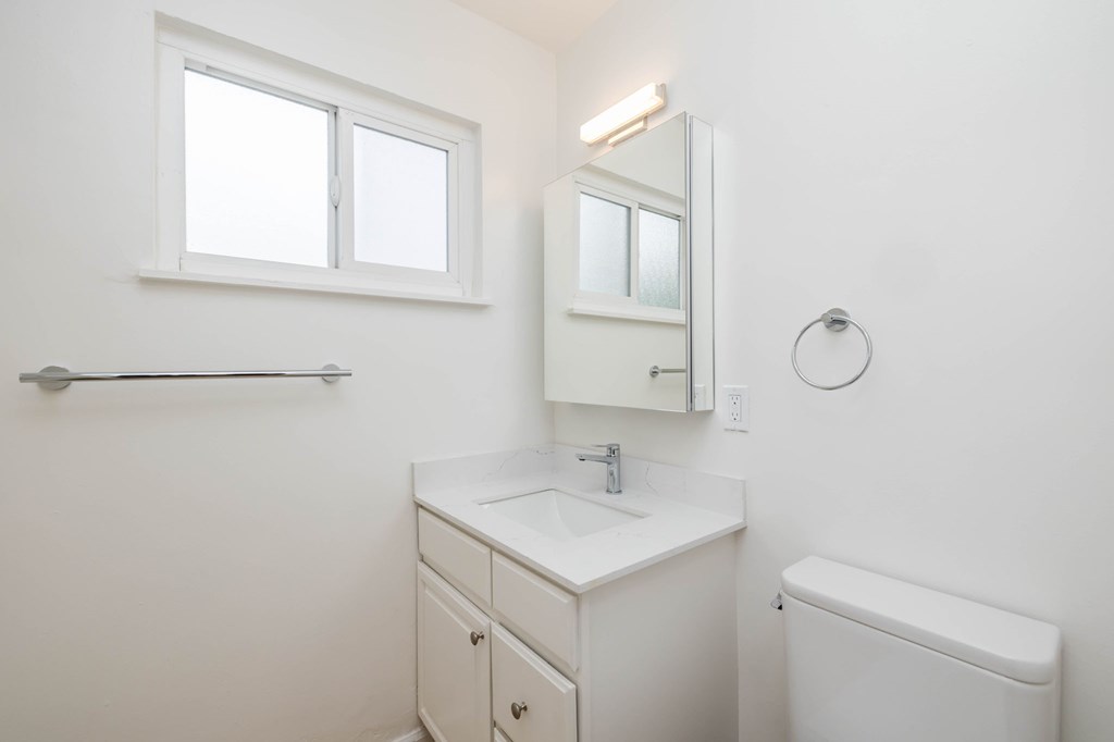 A white bathroom with a sink, mirror, and toilet.