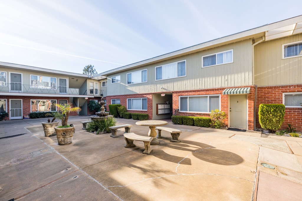 A courtyard with a bench and a tree in front of a building.