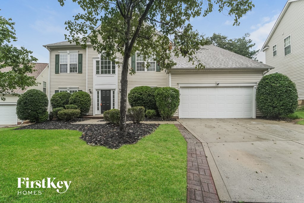 a white house with a driveway and a tree in the yard