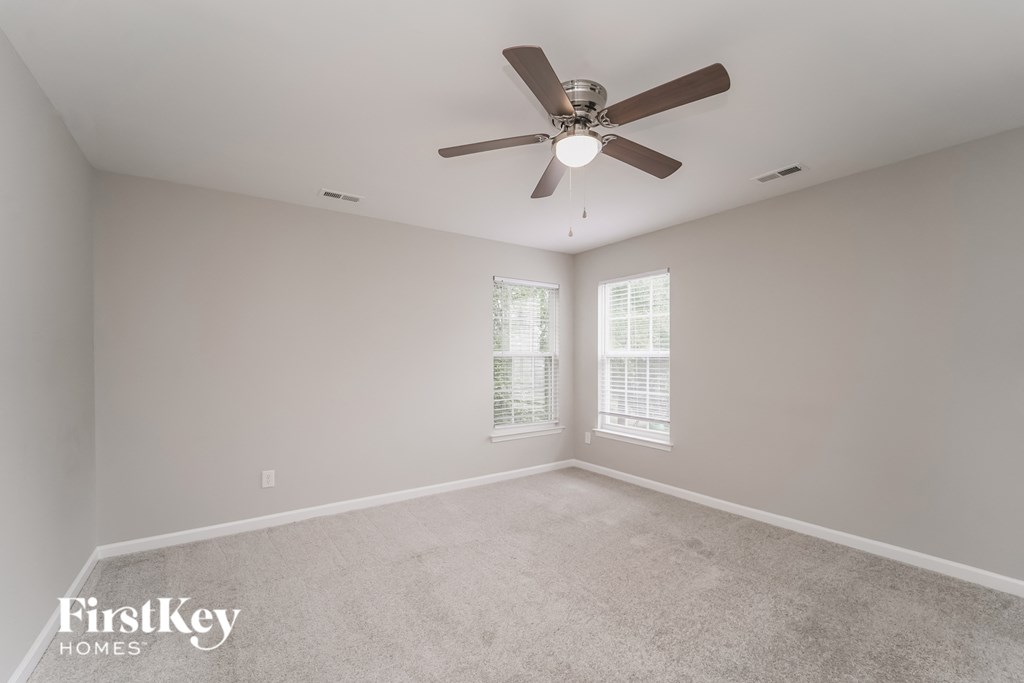 an empty room with a ceiling fan and two windows