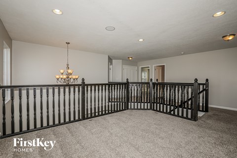 A spacious room with a chandelier and a black railing.