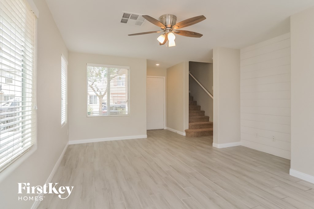 an empty living room with a ceiling fan and a staircase