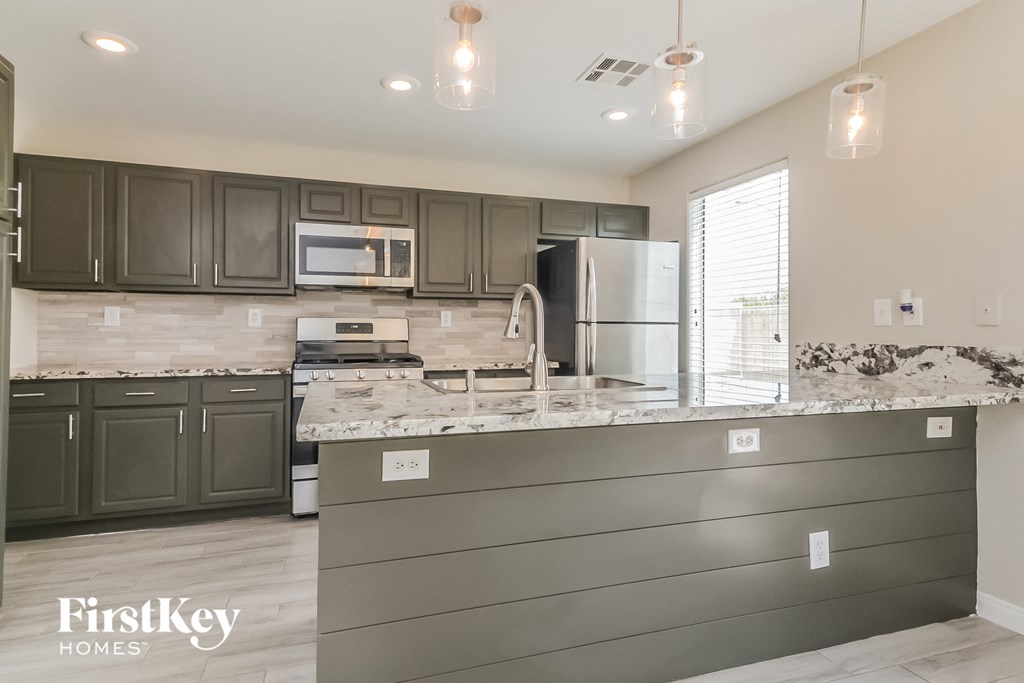 a kitchen with granite counter tops and gray cabinets and stainless steel appliances