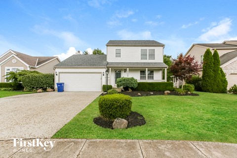 A house with a driveway and a blue trash can in front of it.