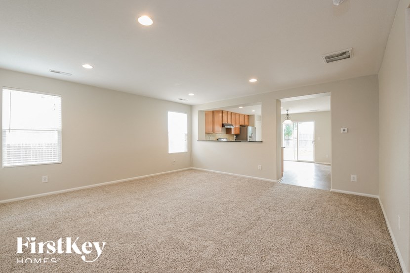 A spacious empty room with a carpeted floor and a kitchen area in the background.
