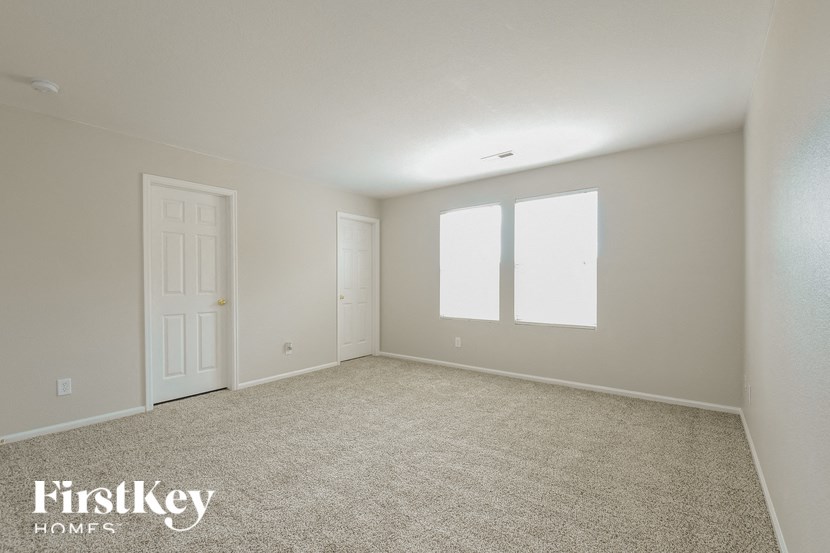 A room with a carpeted floor and a door and two windows.
