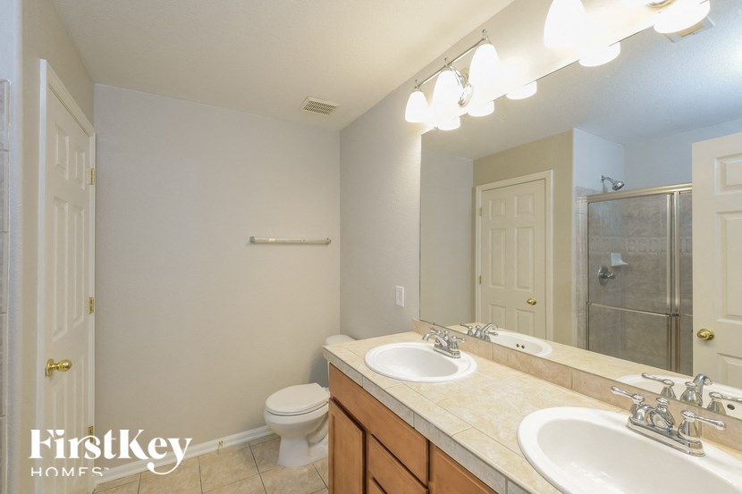 A bathroom with a toilet, sink, mirror and lighting.