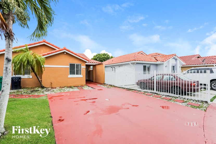 A red brick house with a white fence and a car parked in front.