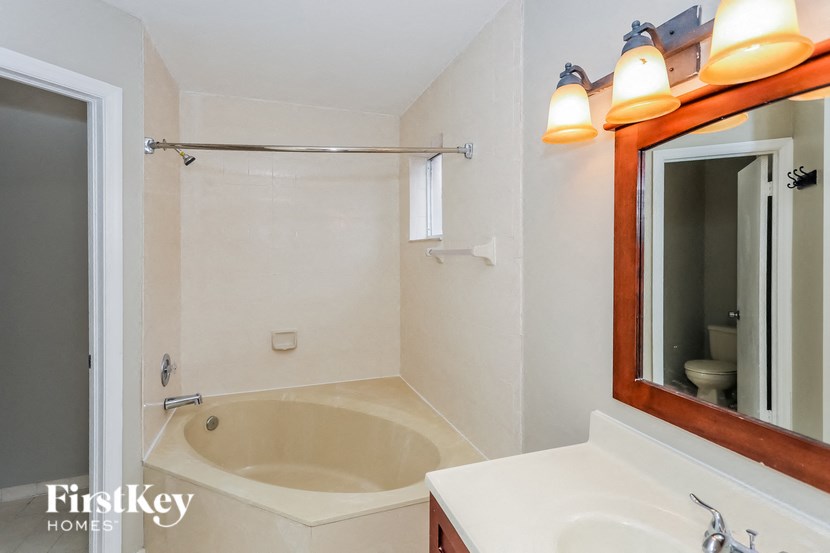 A bathroom with a tub, sink and mirror.