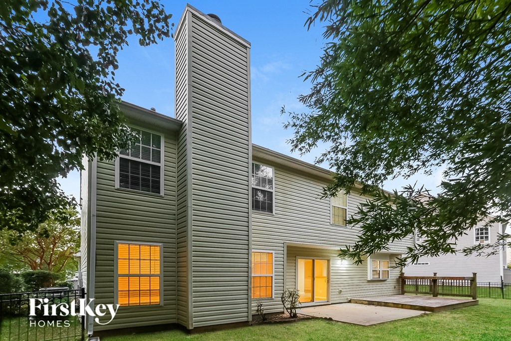 A house with a grey siding and a tall chimney is surrounded by trees.