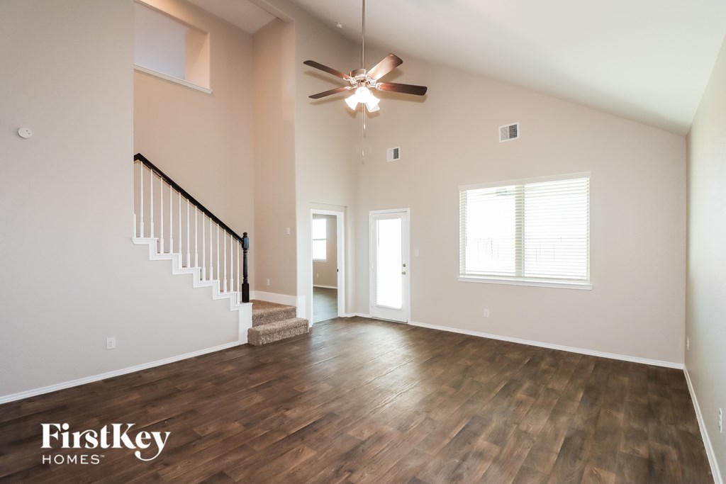 A spacious room with wooden floors and a staircase leading to the upper level.