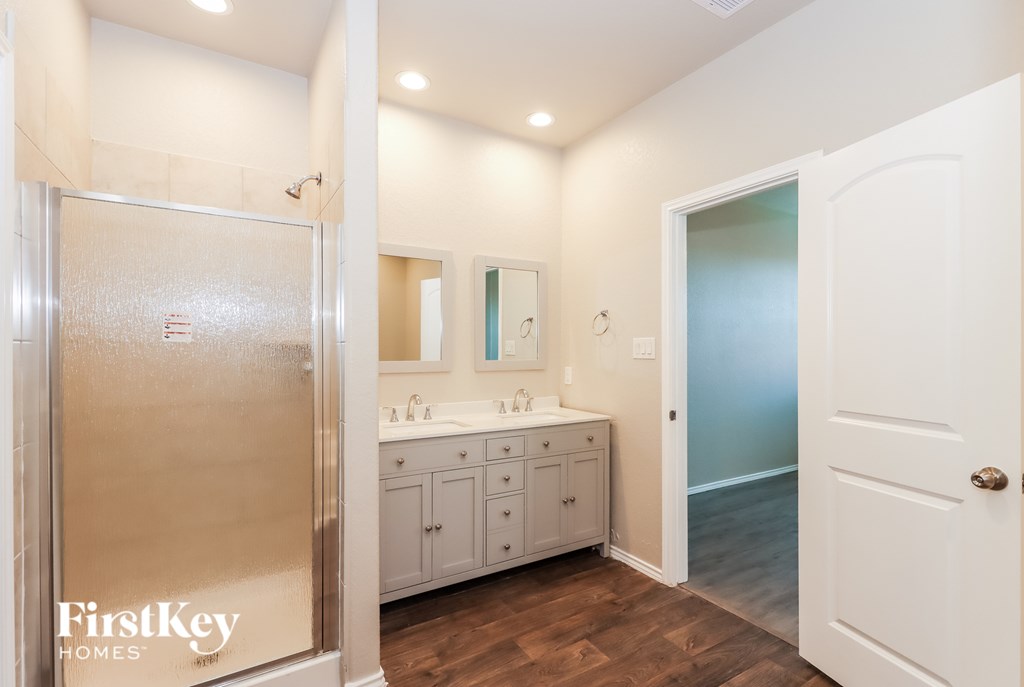 A bathroom with a walk-in shower, double sinks, and a wooden floor.
