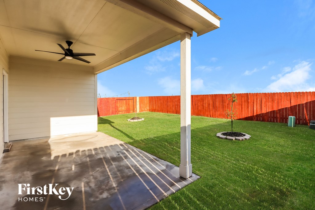 A patio with a ceiling fan and a view of a red fence.