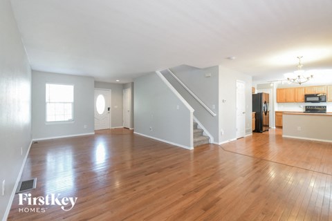 A spacious living room with wooden floors and a staircase leading to the upper level.