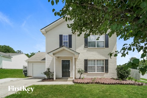A house with a white facade and a black door is surrounded by greenery.