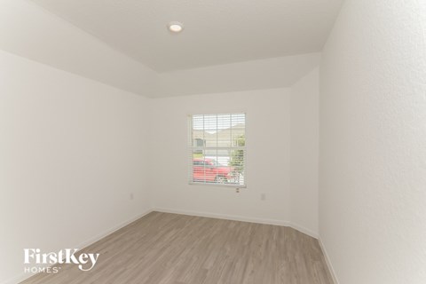 a bedroom with white walls and wood floors and a window