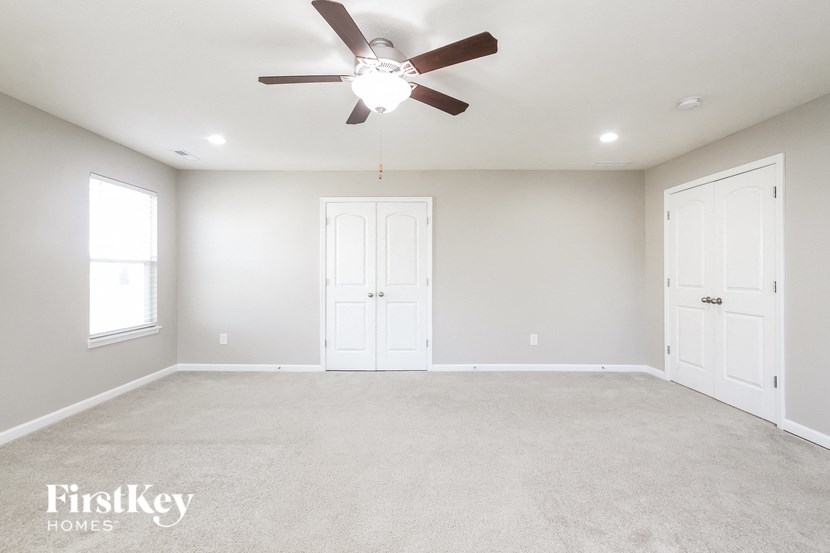 A spacious room with a ceiling fan and three doors.