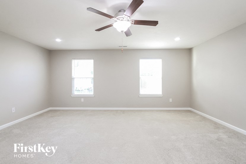 A spacious room with a ceiling fan and two windows.