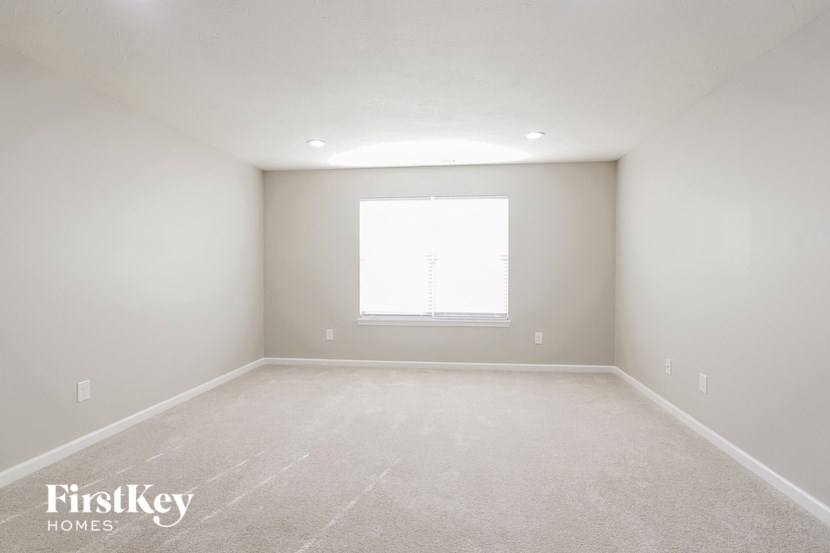 A spacious empty room with a window and carpeted floor.